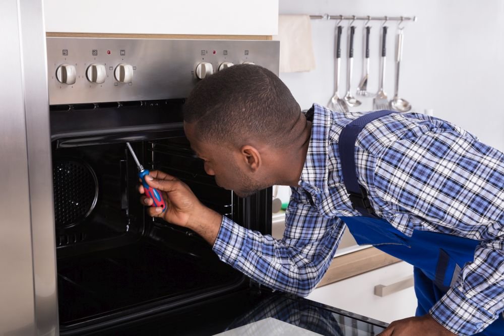Young Repairman With Screwdriver Fixing Kitchen Oven